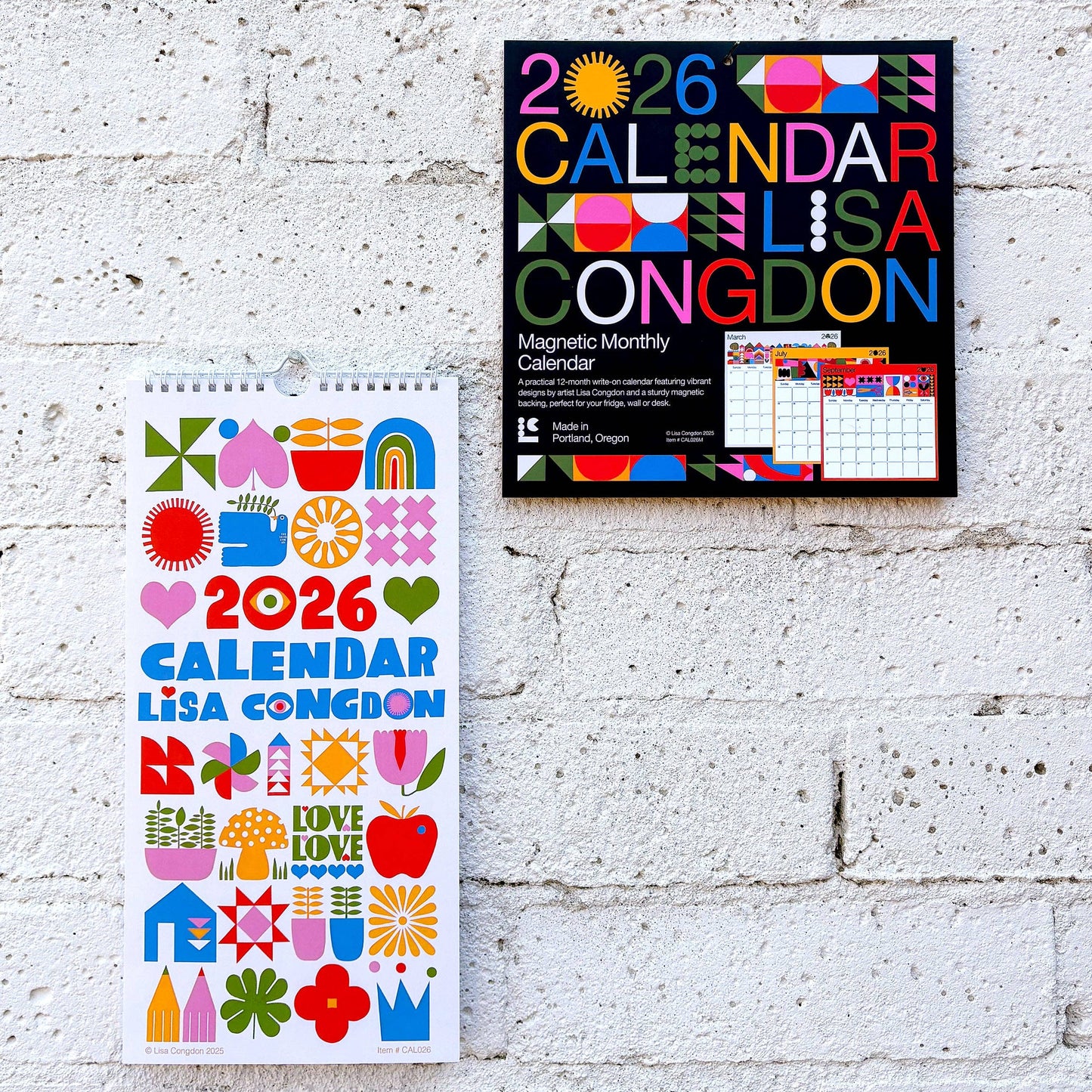Two Lisa Congdon 2026 calendars, one wall-mounted and one standing, against a white brick wall.