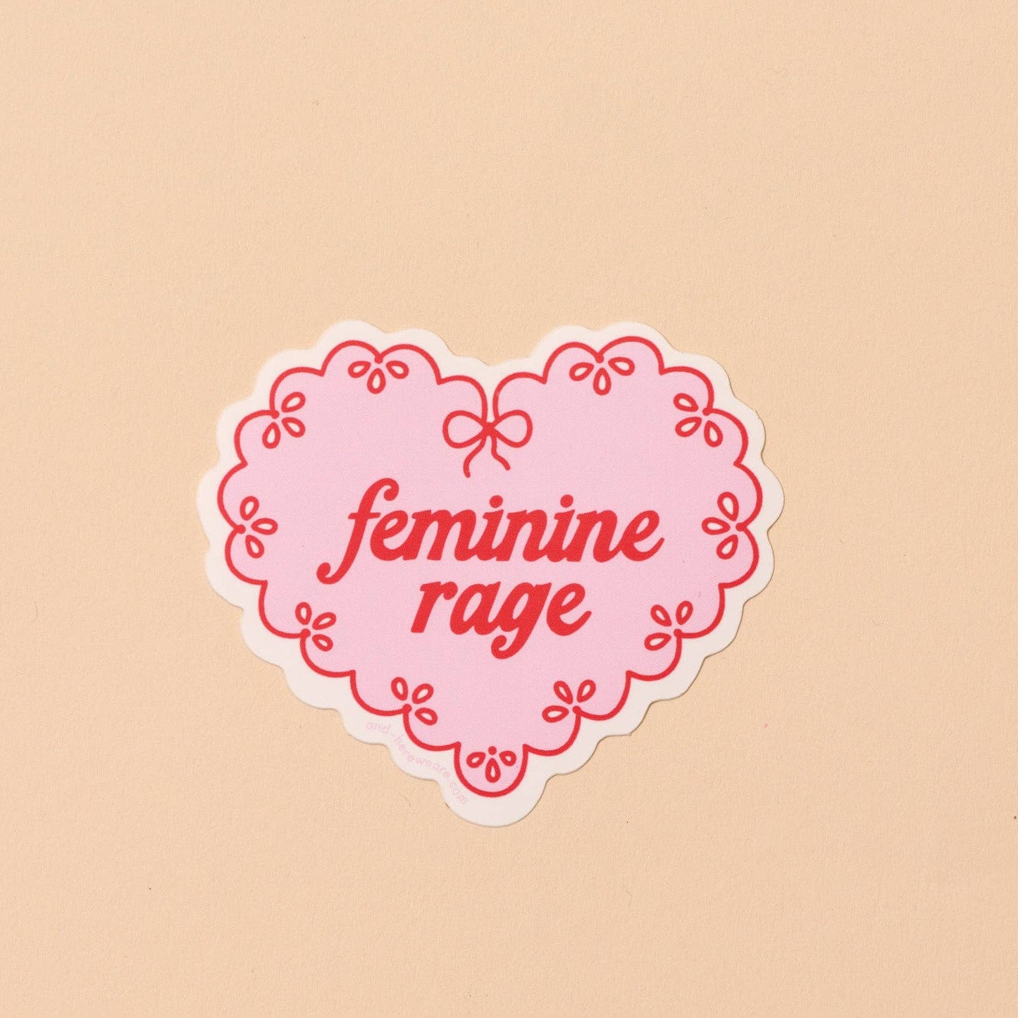 Heart-shaped sticker with 'feminine rage' text on a beige background