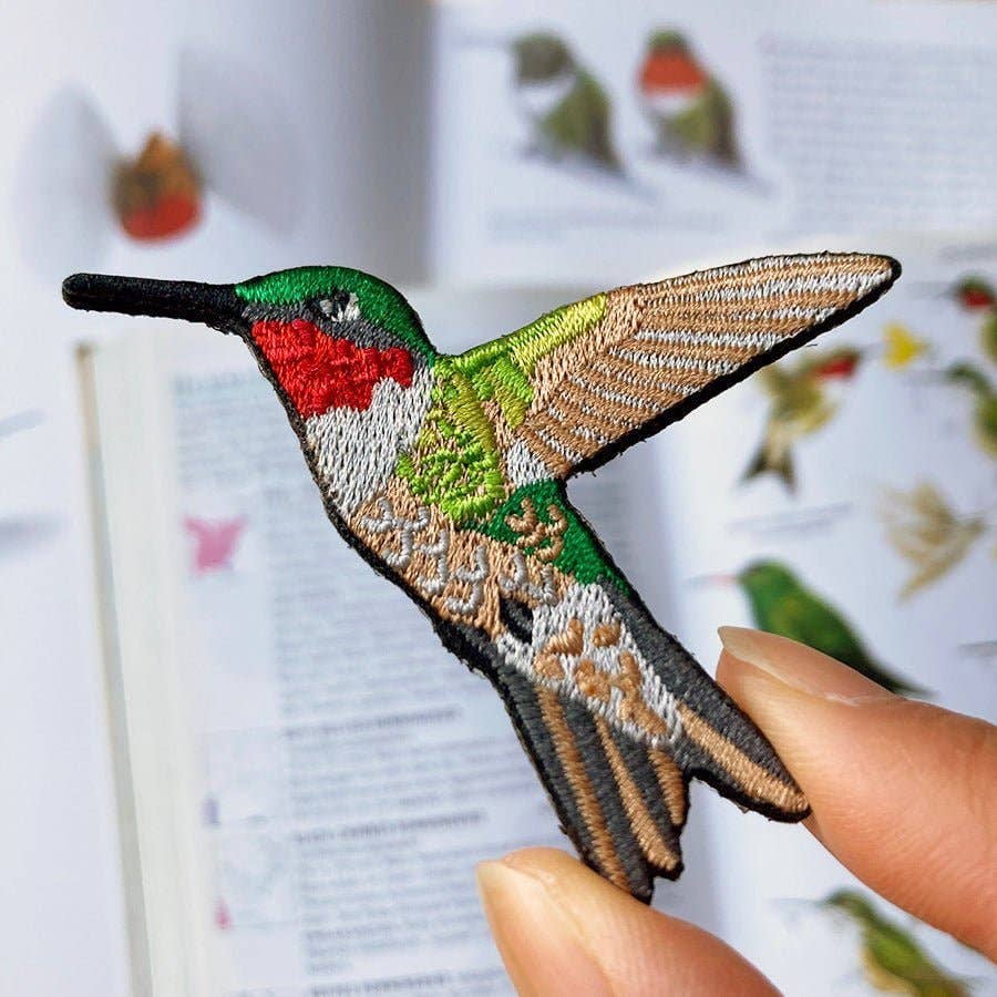 Embroidered patch of a hummingbird held by a hand with a blurred background