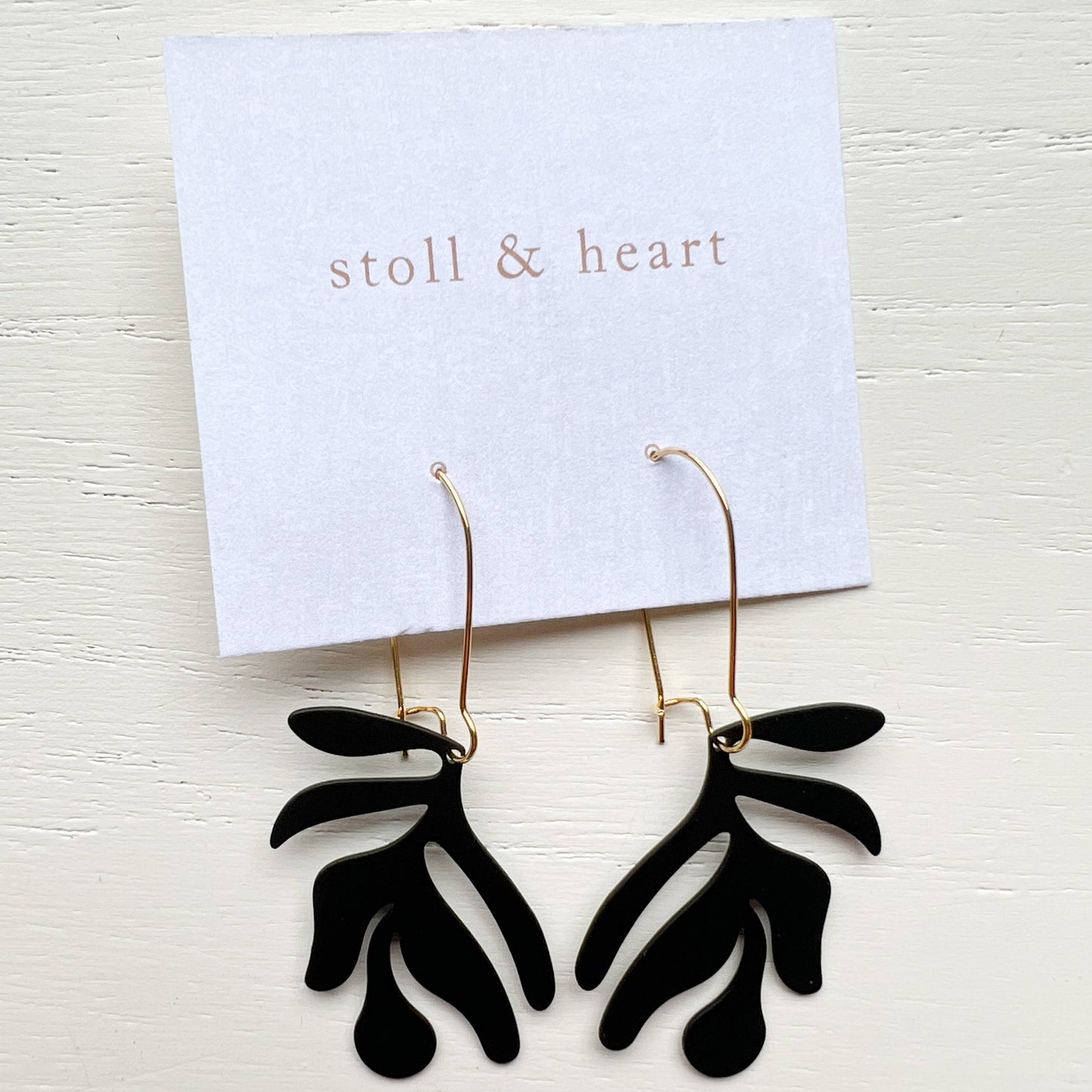 Black leaf-shaped earrings on a 'stoll & heart' branded card against a white background