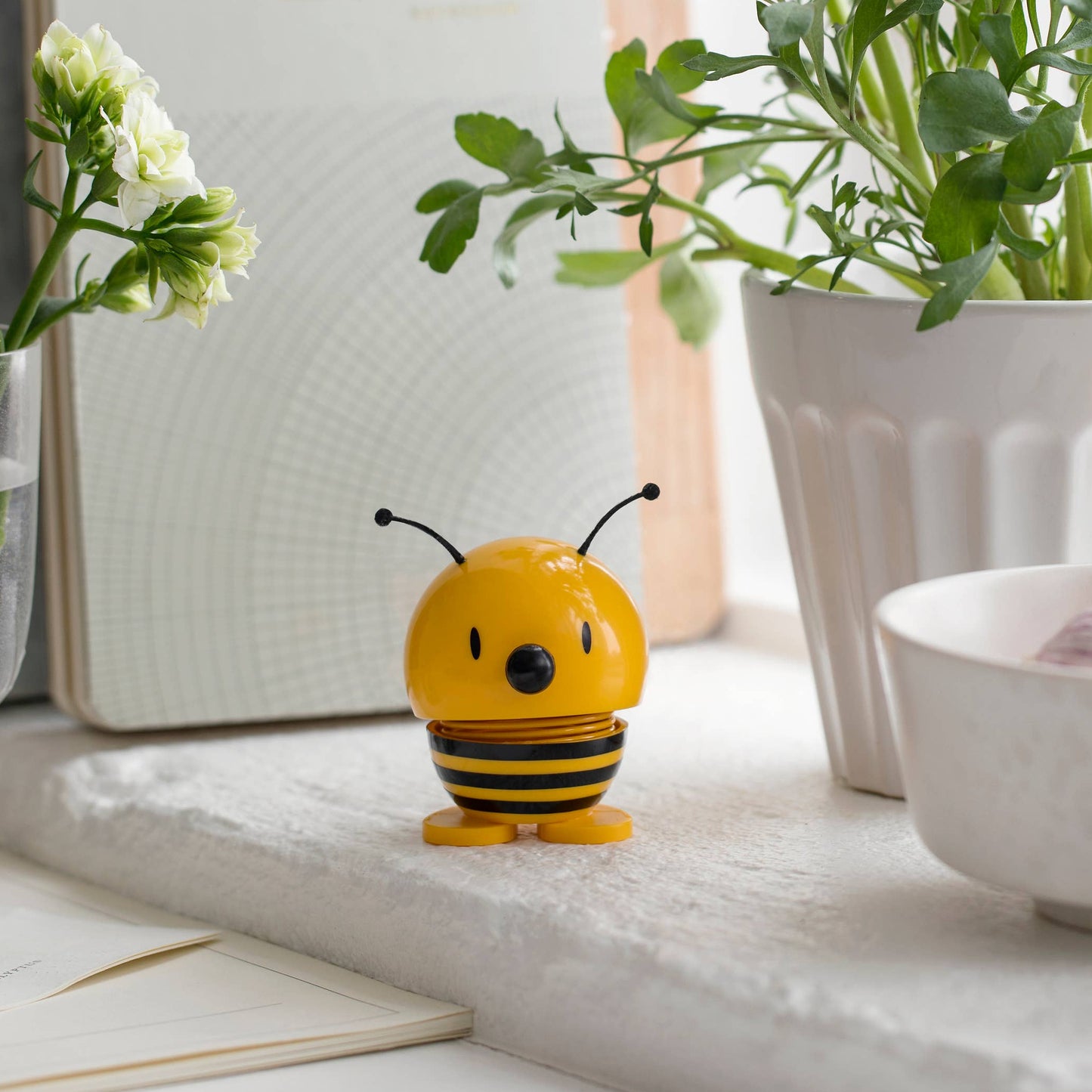 Small bee figurine on a windowsill with plants and books in the background