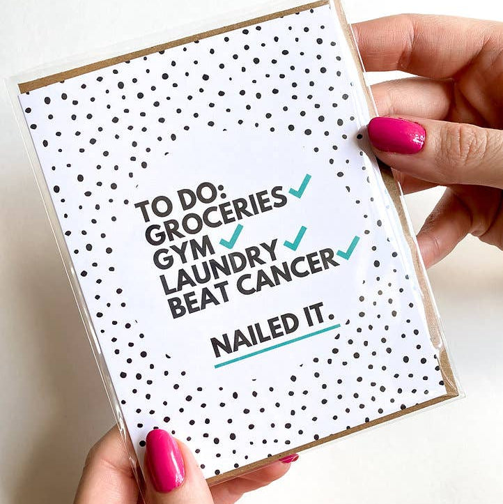 Card with text 'To Do: Groceries, Gym, Laundry, Beat Cancer. Nailed It.' held by a person with pink nails.