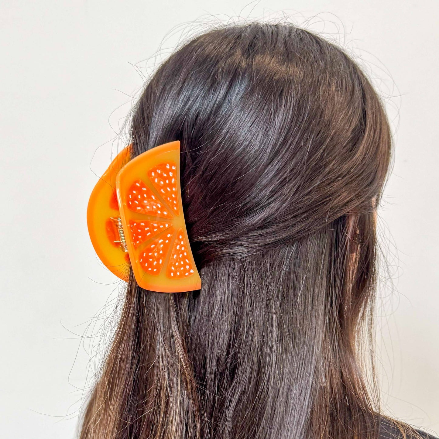 Orange hair clip with a fruit design in a person's hair on a light background