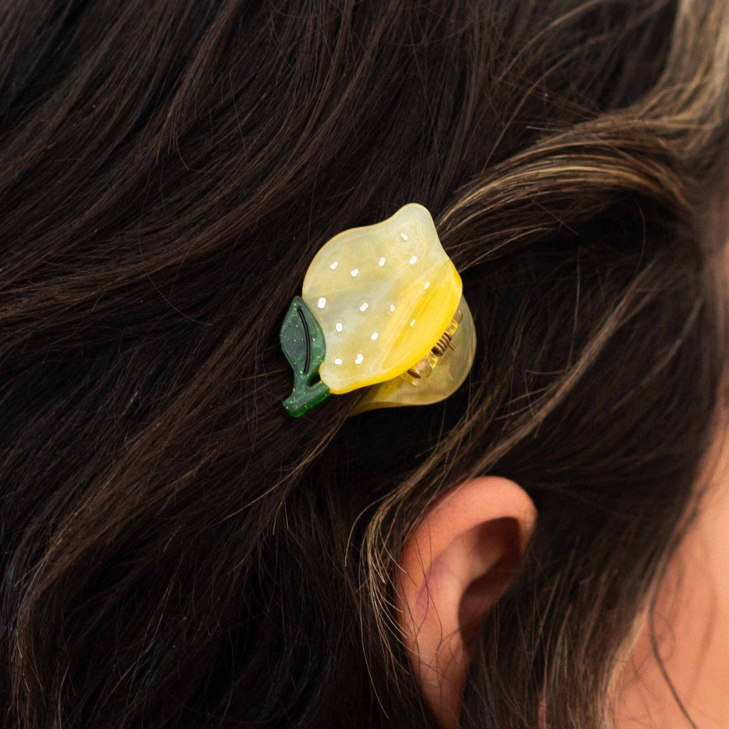 Yellow hair clip with green leaves attached to dark hair