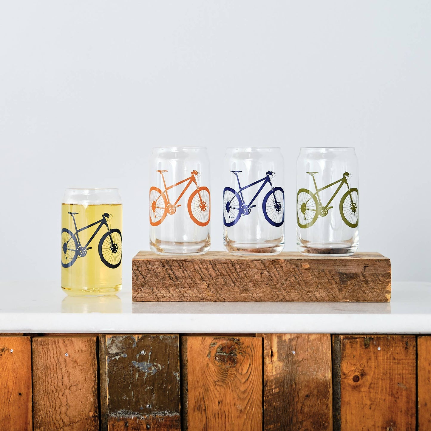 Four bicycle-themed glasses on a wooden block with a white background