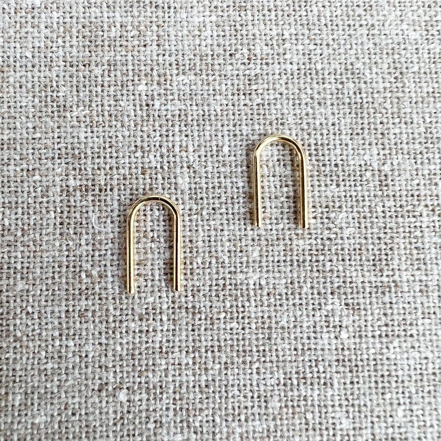 Gold U-shaped earrings on a textured gray fabric background