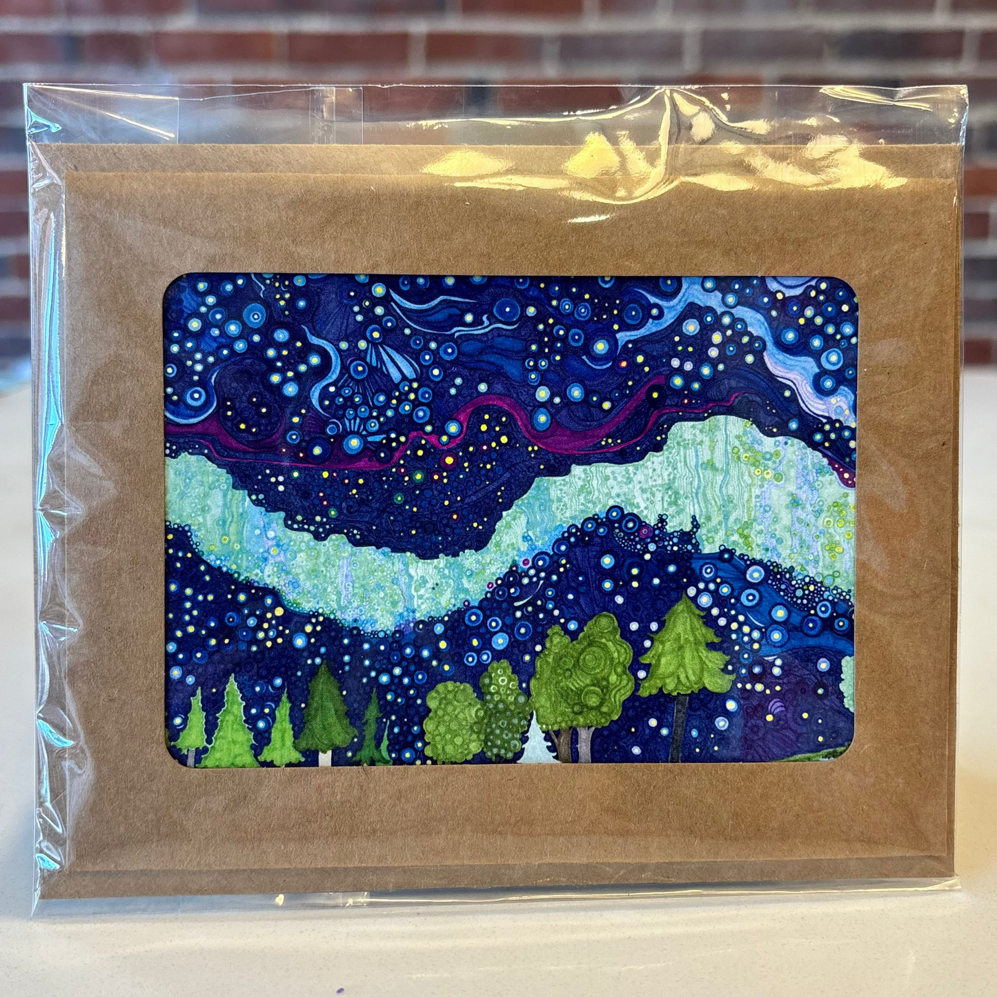 Greeting card with a starry night design in a clear plastic sleeve against a brick wall background.