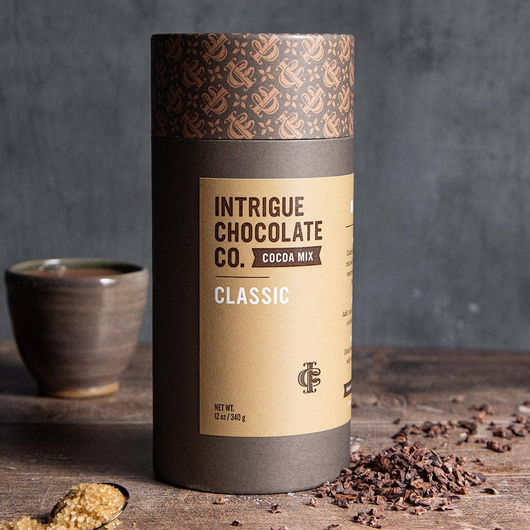 Intrigue Chocolate Co. cocoa mix container on a wooden surface with a dark background