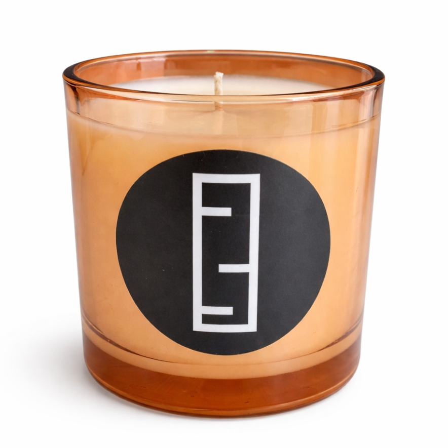 Candle in an amber glass jar with a black label featuring a white logo on a white background