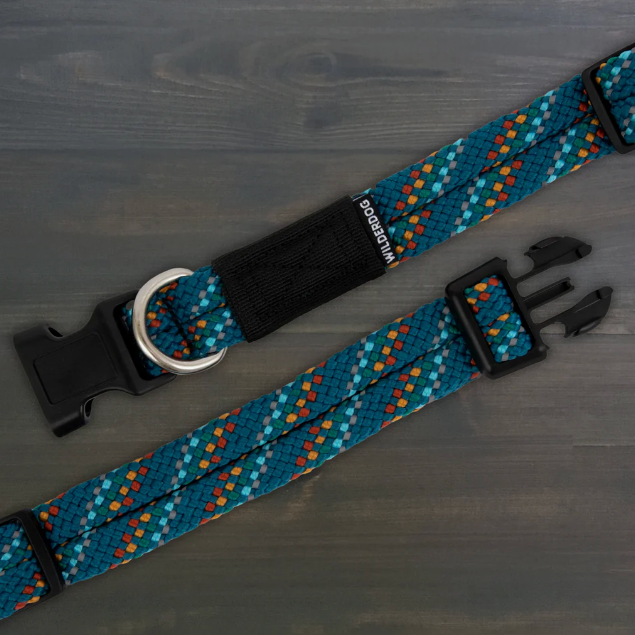 A dog collar with a blue, teal, orange, and white geometric pattern, featuring black plastic buckles and a black velcro patch with the brand name 'Pup Power' printed on it, displayed on a dark gray wood background.