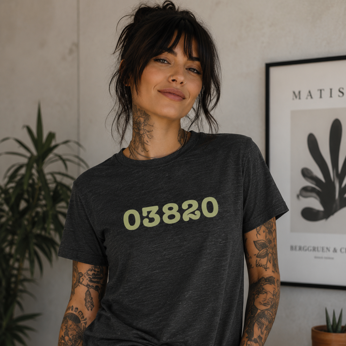 Person wearing a dark gray t-shirt with '03820' printed in green, standing indoors.