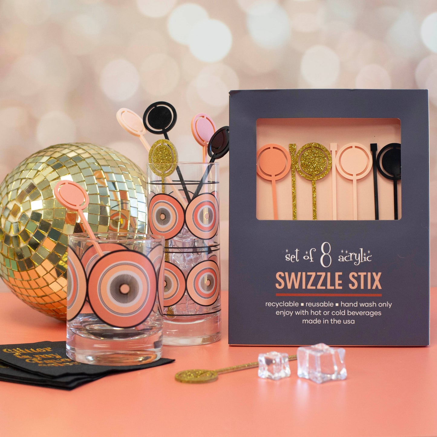 Set of swizzle sticks in a box with glasses and disco ball on a pink surface