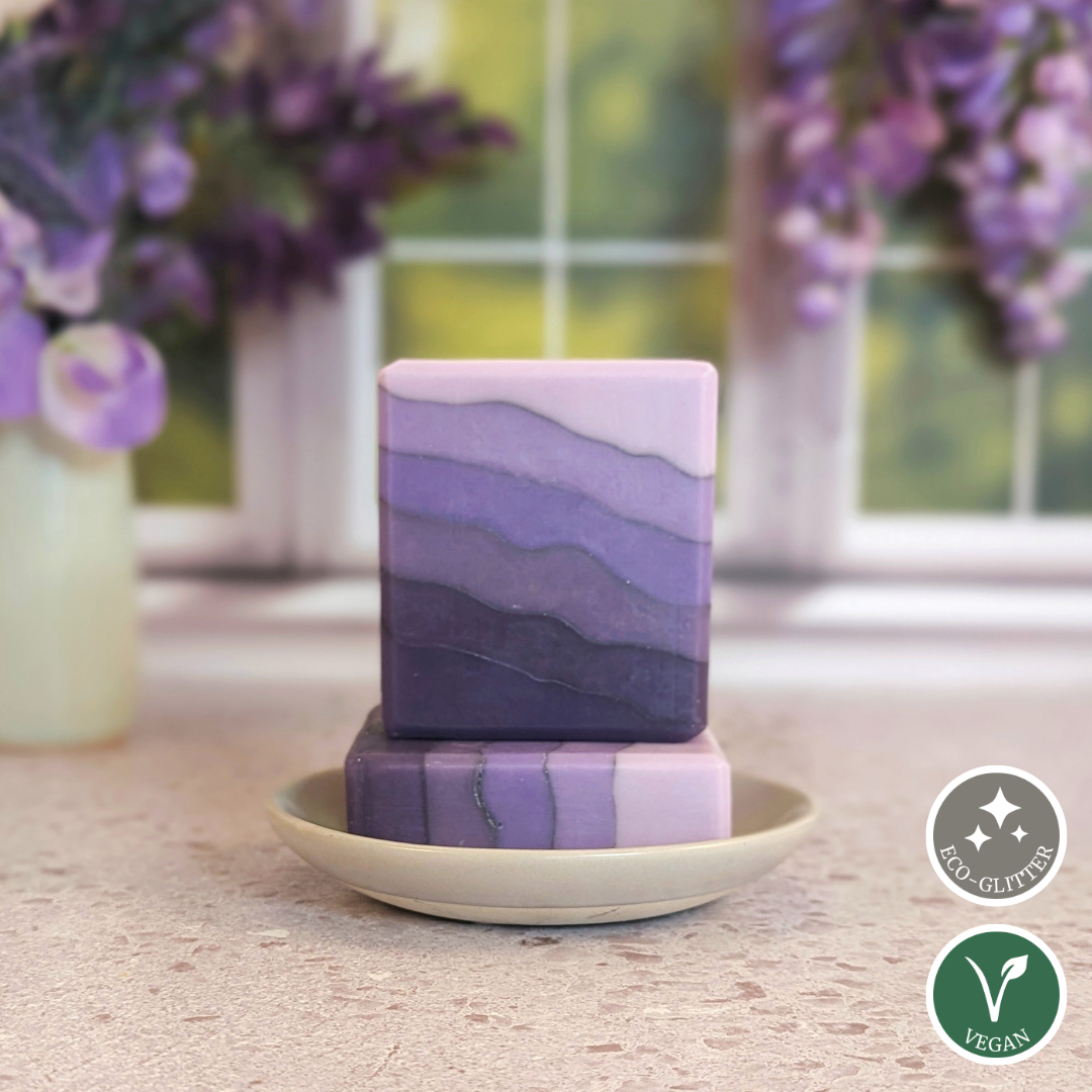 Two stacked purple soap bars on a beige plate with lavender flowers in the background.