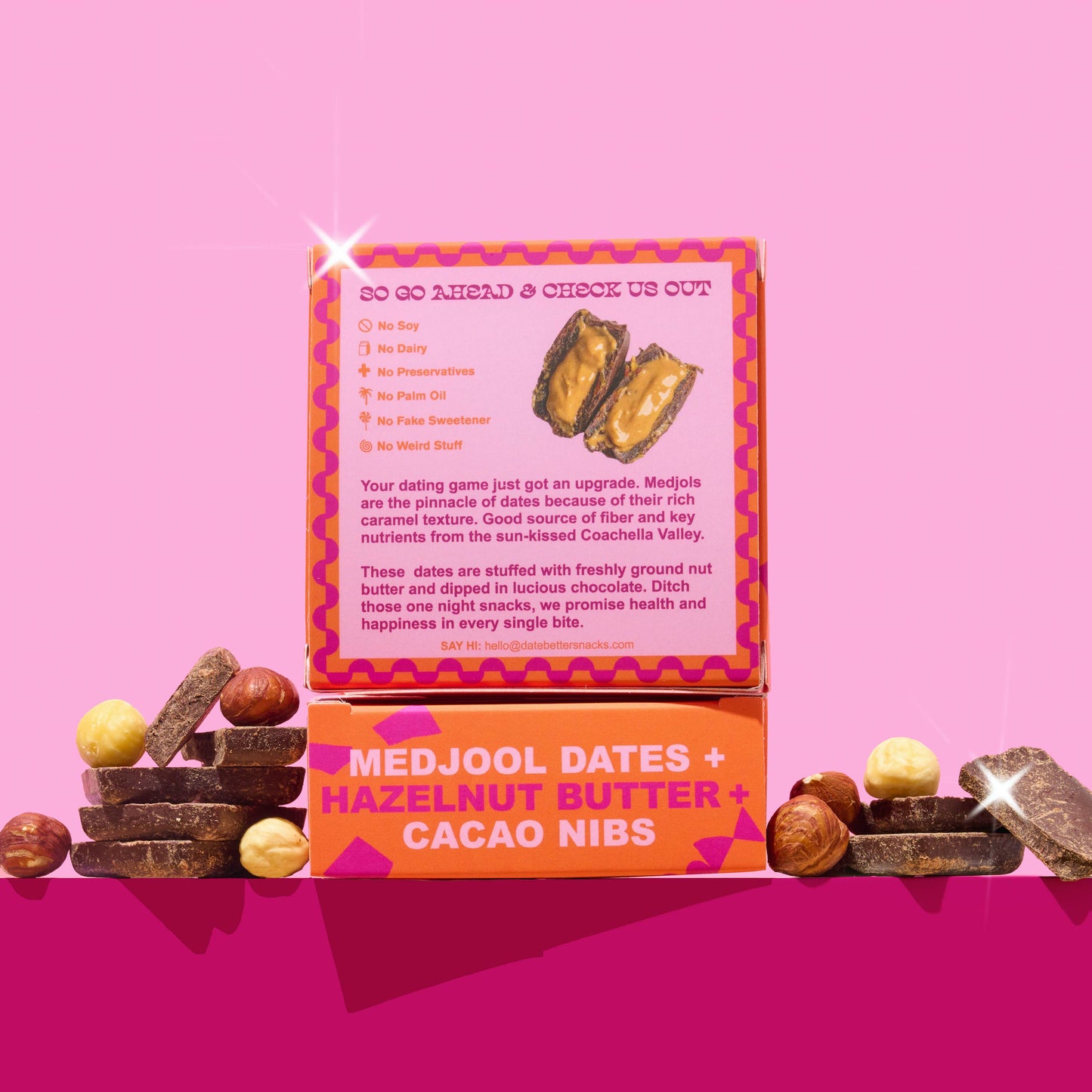 Box of Medjool dates, hazelnut butter, and cacao nibs on a pink background