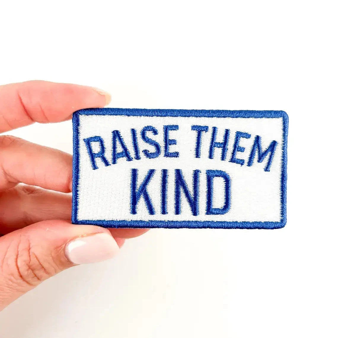 Patch with 'Raise Them Kind' text held by a hand on a white background