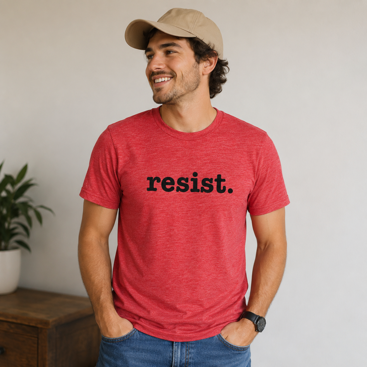 Man wearing a red t-shirt with 'resist.' text, standing indoors.