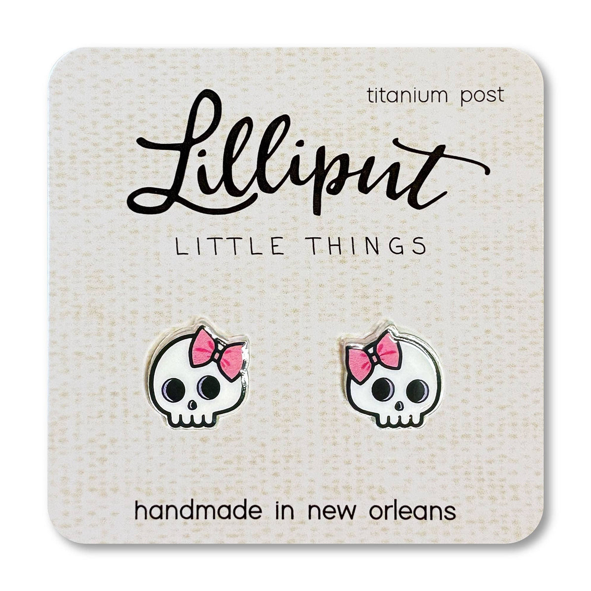 Skull-shaped earrings with pink bows on a Lilliput Little Things branded card.