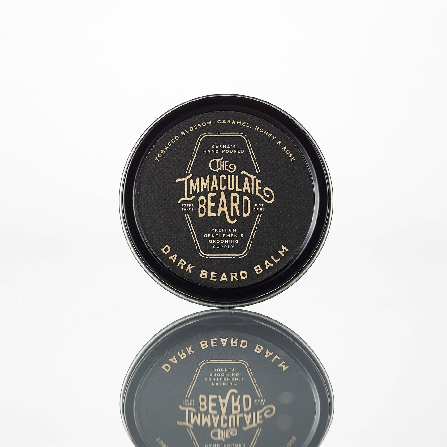Dark-colored beard balm container with 'The Immaculate Beard' branding on a white background