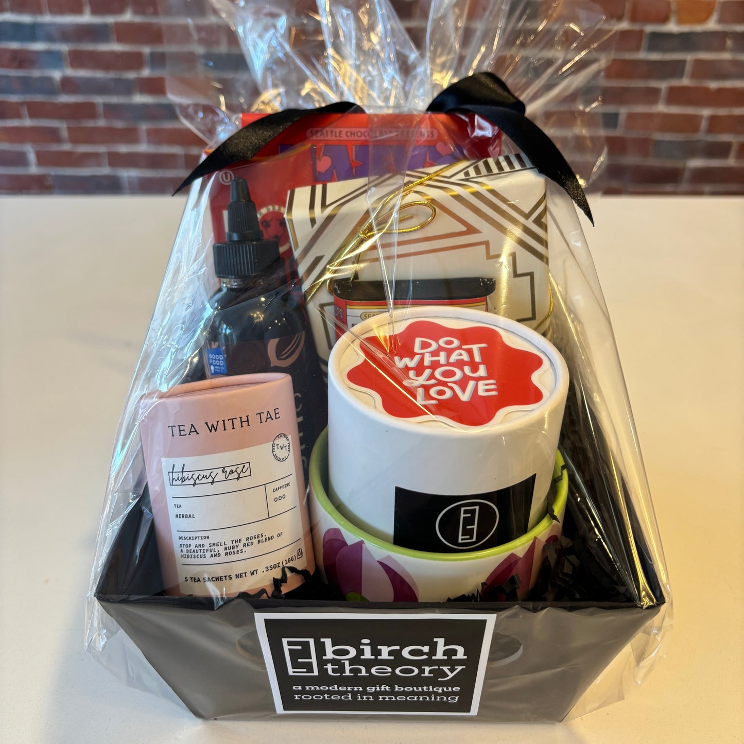 Gift set with products including a bottle, container, and card, branded with 'birch theory', on a white surface with a brick wall background.