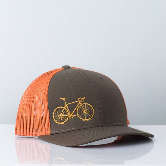 Trucker hat with orange mesh back and brown front, featuring a yellow bicycle emblem on a light gray background.