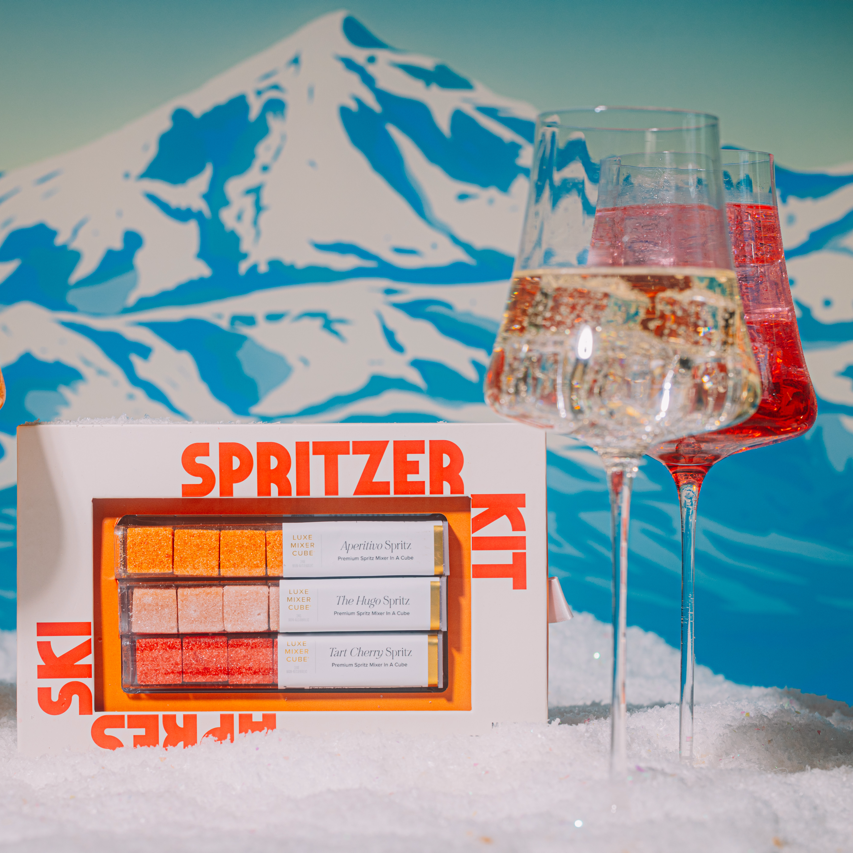 Spritzer kit with glasses of orange and red drinks against a mountainous background