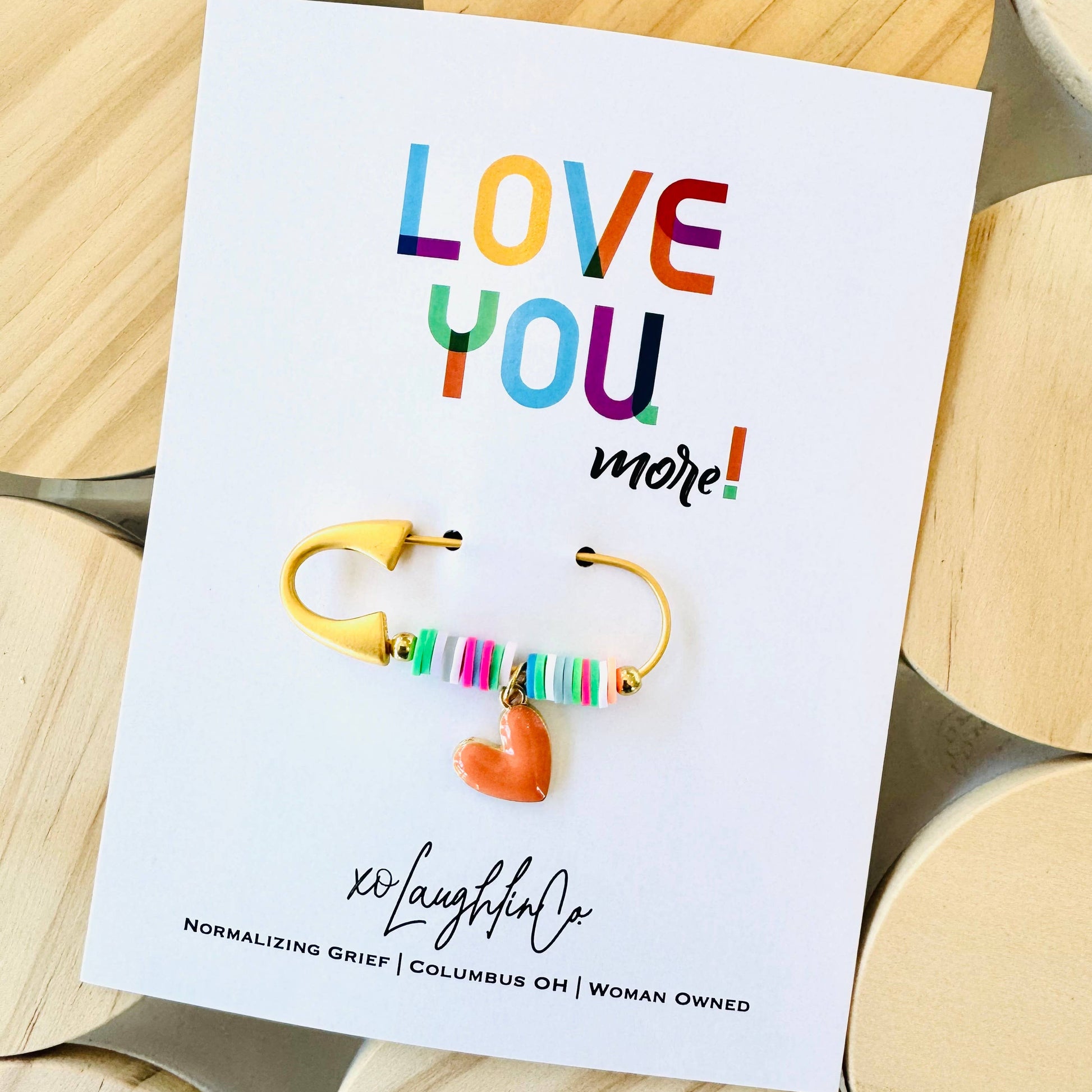 Colorful earrings on a card with 'LOVE YOU more!' text, displayed on wooden blocks.