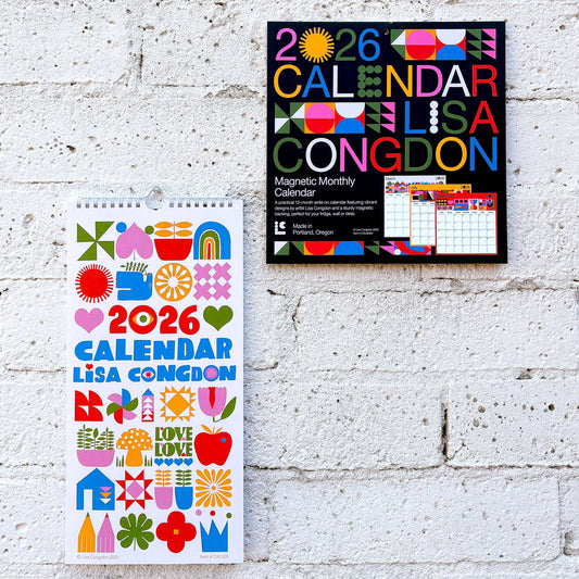 Two Lisa Congdon 2026 calendars, one wall-mounted and one standing, against a white brick wall.