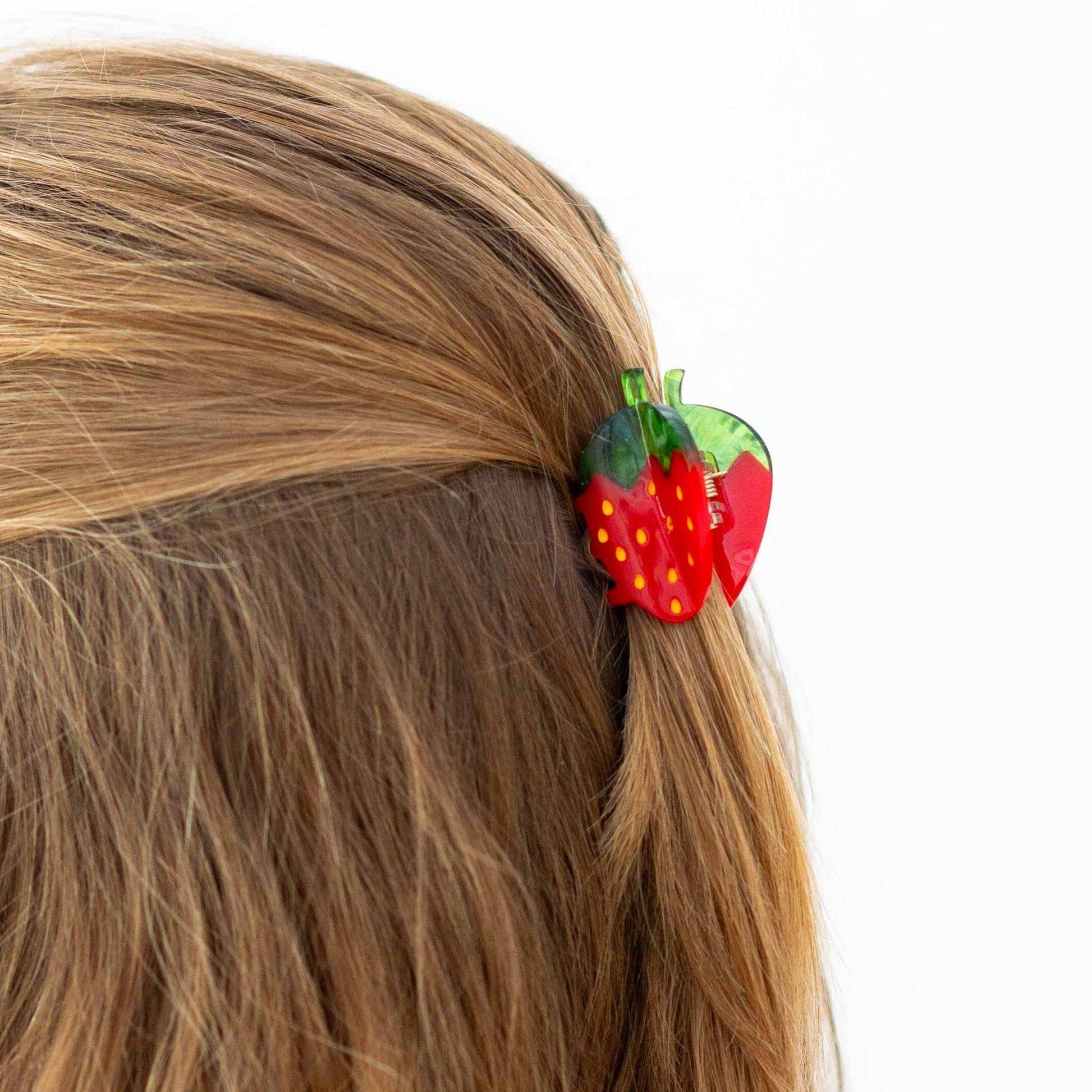 Strawberry-shaped hair clip on a person's hair against a white background