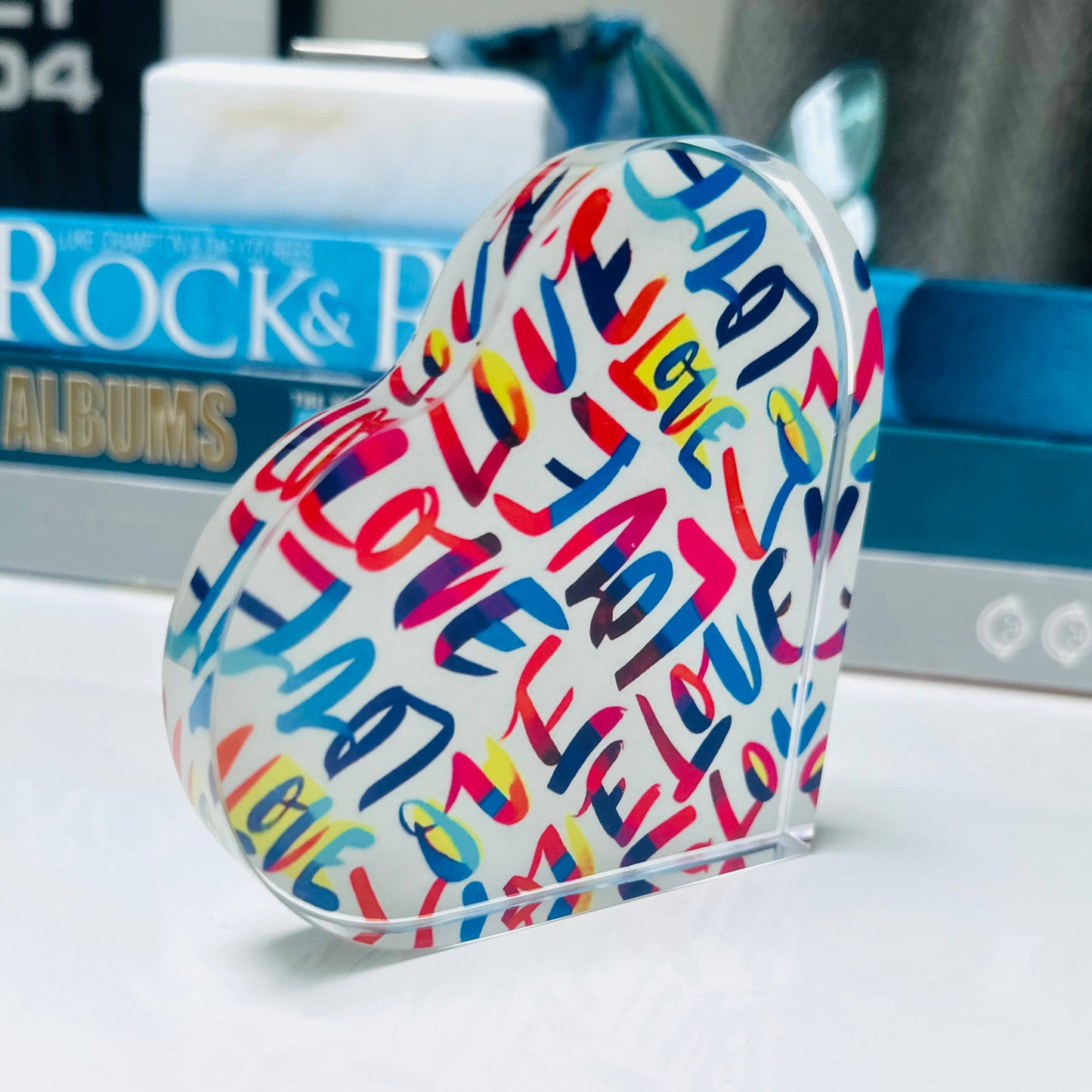 Colorful heart-shaped object with text on a surface with books in the background