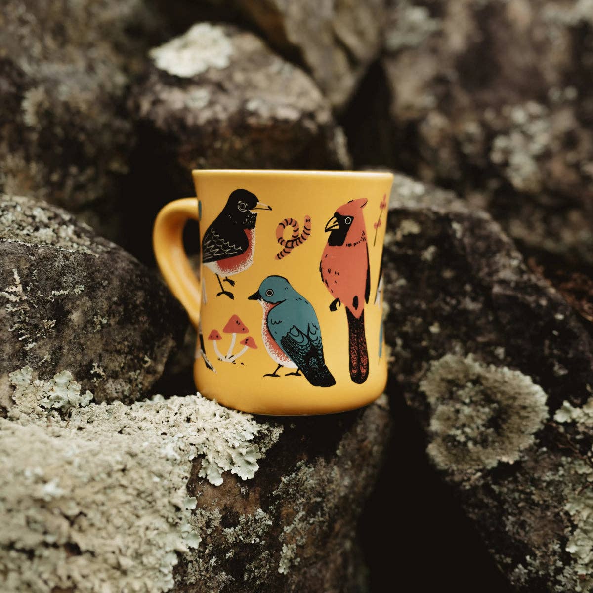 Yellow mug with bird designs on a textured stone surface