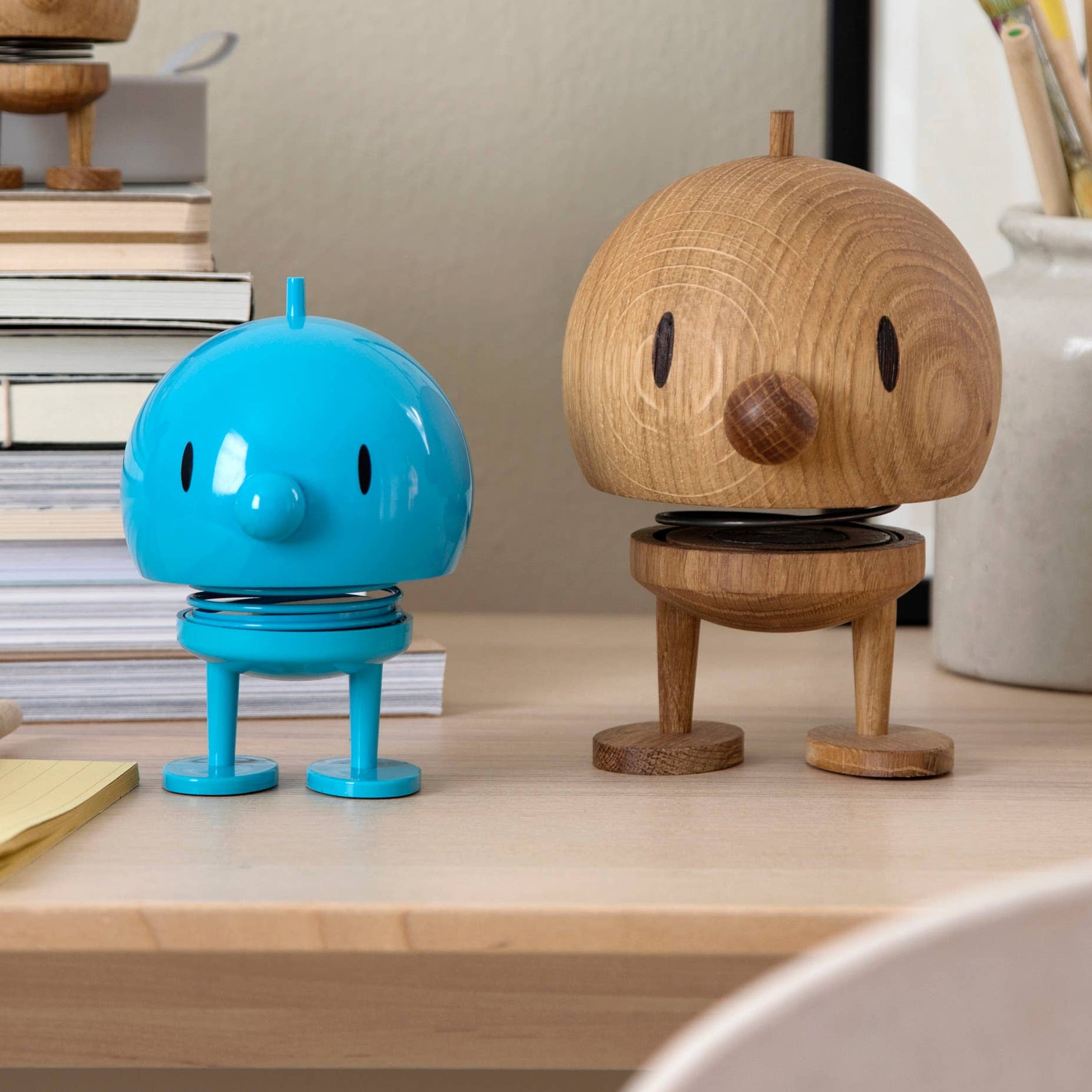 Two small figurines, one blue and one brown, on a desk with books and stationery in the background.