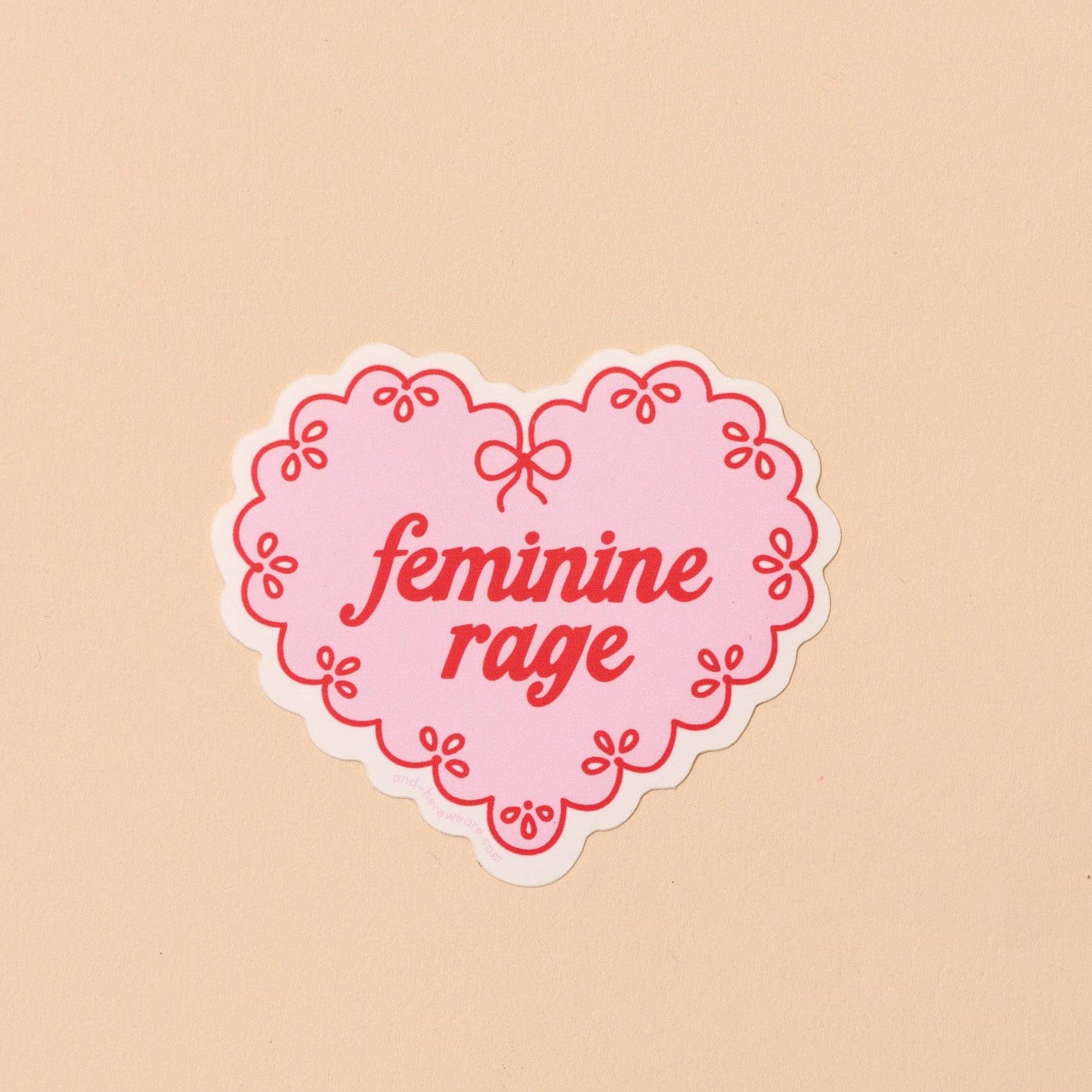 Heart-shaped sticker with 'feminine rage' text on a beige background