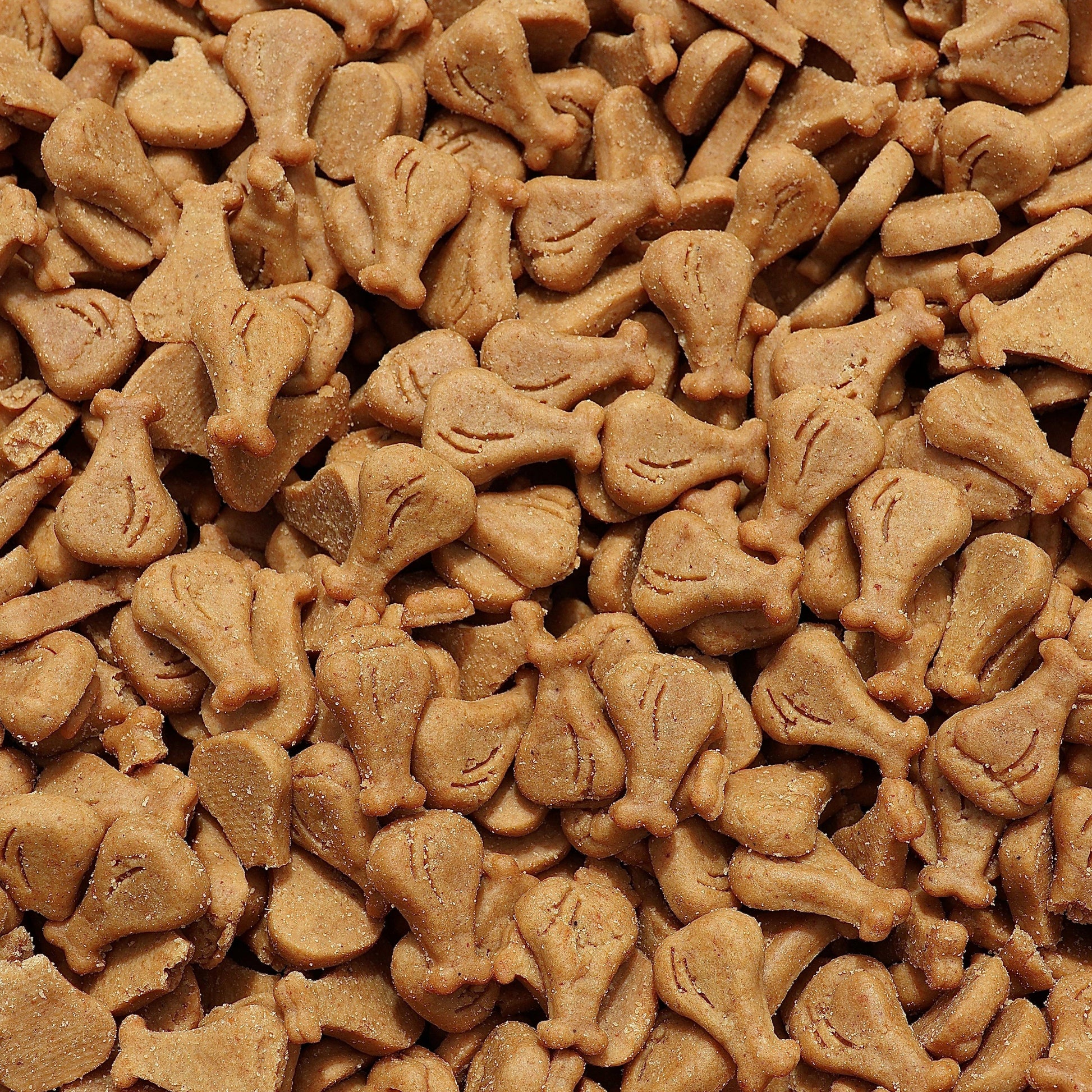 A close-up, top-down view of small, brown, dog-shaped treats or biscuits densely packed together.
