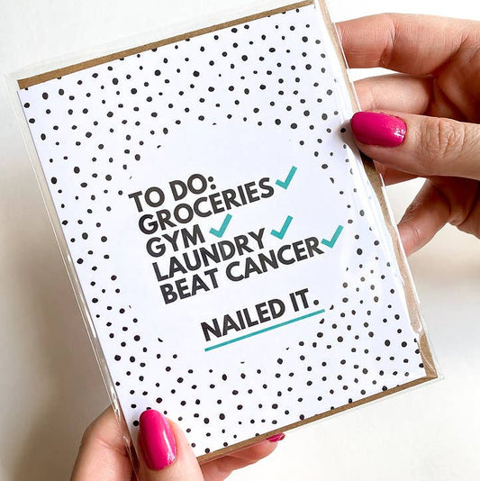 Card with text 'To Do: Groceries, Gym, Laundry, Beat Cancer. Nailed It.' held by a person with pink nails.