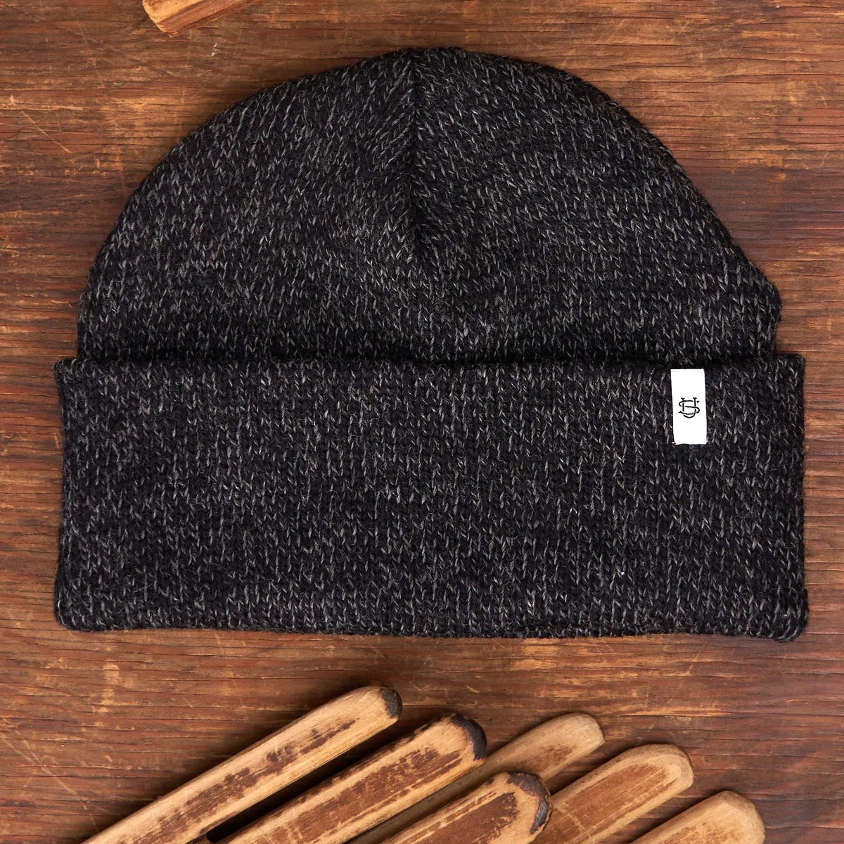 Black knit beanie with a brand tag on a wooden surface