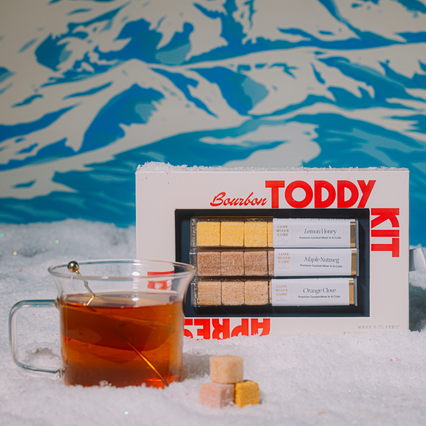 Bourbon Toddy Kit with a glass of amber liquid on a snowy background