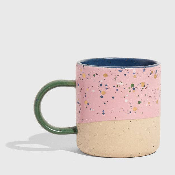 Pink speckled mug with a green handle on a light gray background