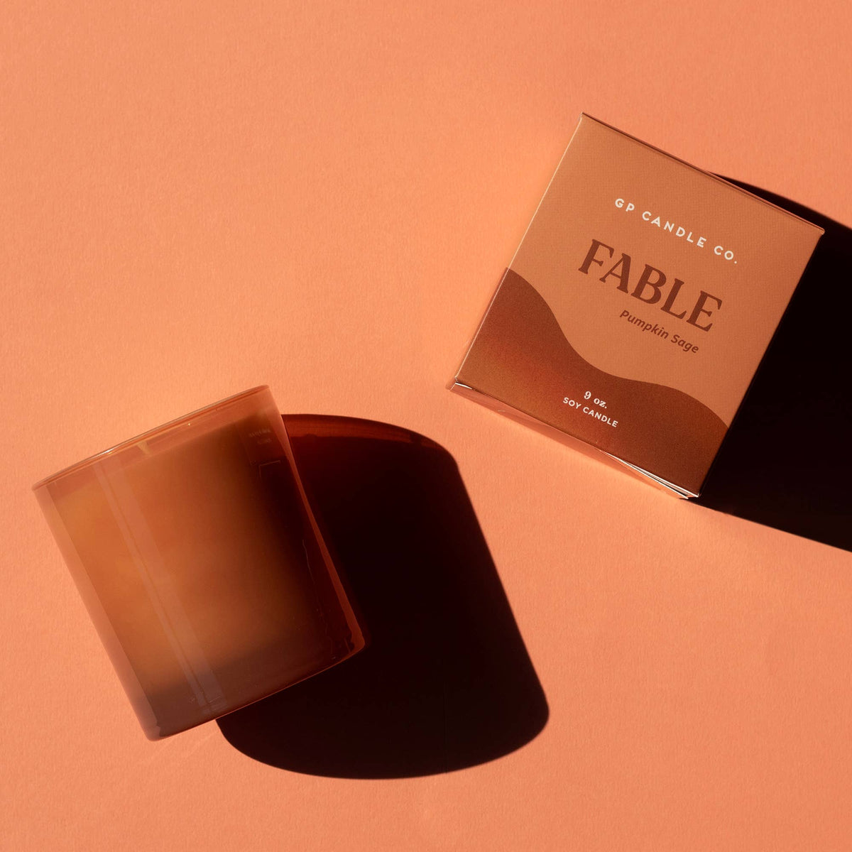 A 5-oz soy candle by FP Candle Co. in a translucent amber glass jar, shown next to its matching square packaging box on a warm peach background.