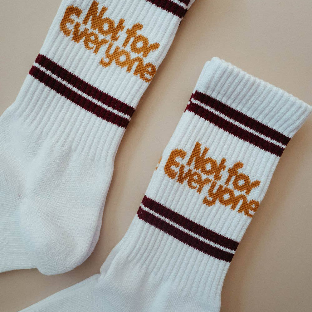 A pair of white crew socks with dark burgundy stripes near the cuff and the words 'Not for Everyone