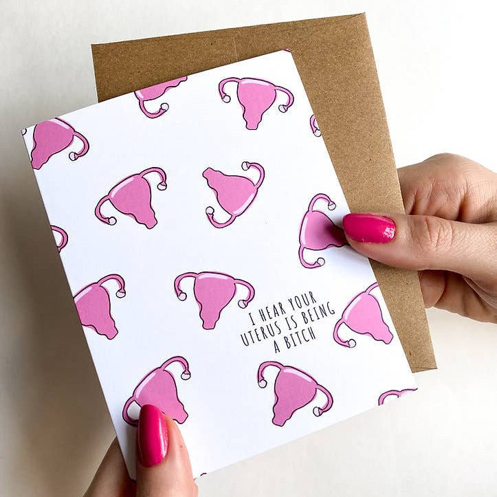 Card with pink uterus illustrations and text held by a person.