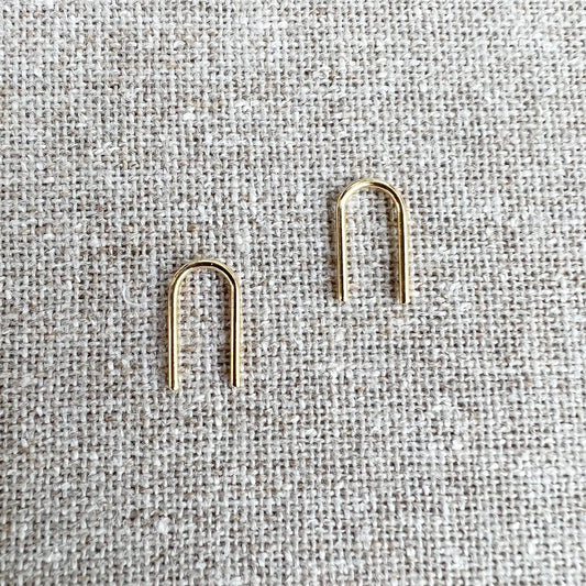 Gold U-shaped earrings on a textured gray fabric background
