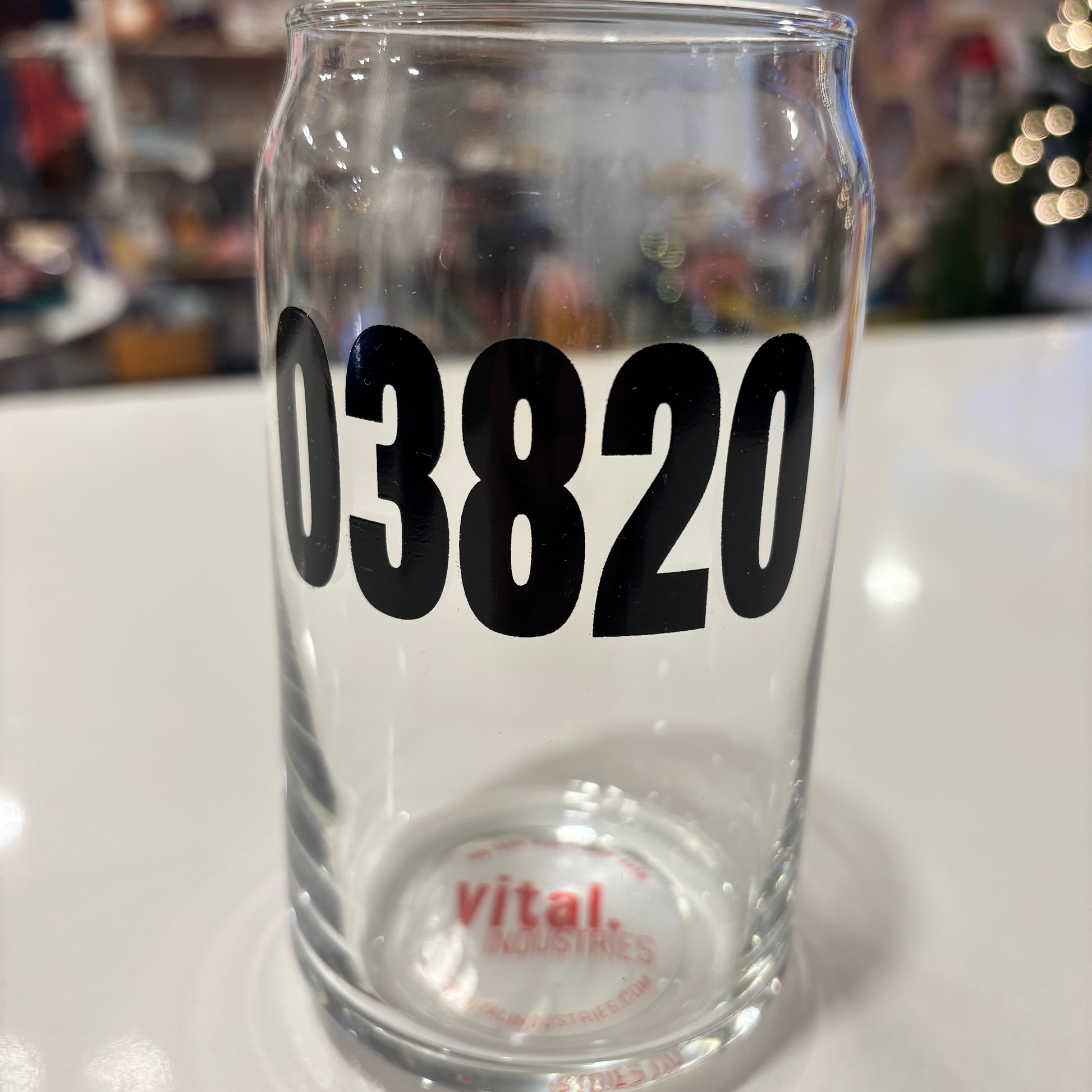 Clear glass tumbler with '03820' printed on it, featuring a blurred background.