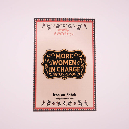 Iron on patch with 'More Women in Charge' text and decorative border on a light pink background