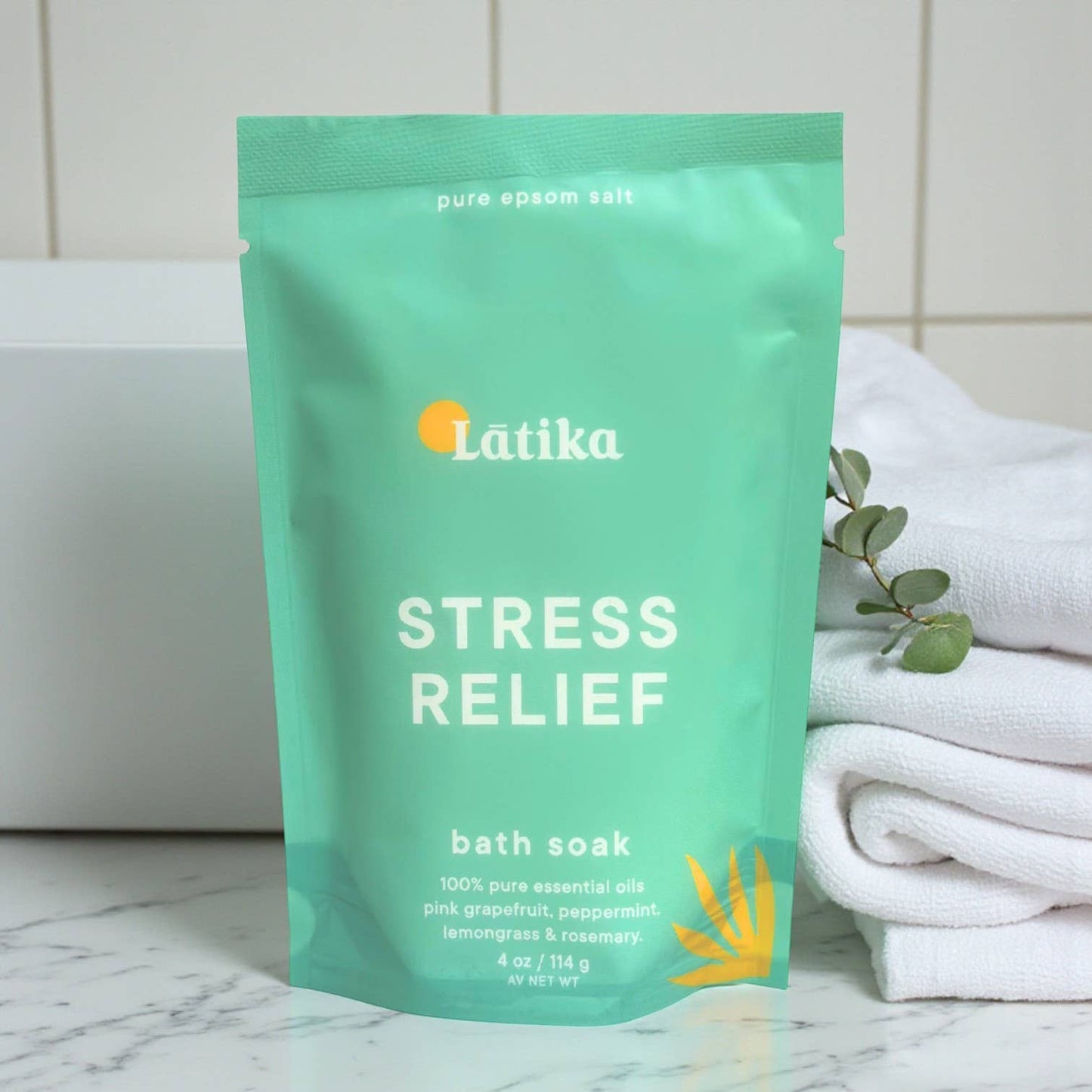 Látika Stress Relief bath soak package on a marble surface with towels and eucalyptus leaves.