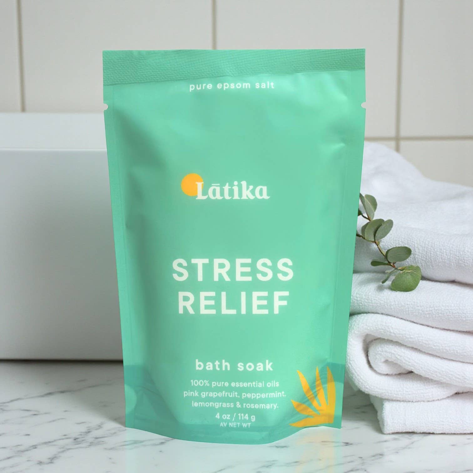 Látika Stress Relief bath soak package on a marble surface with towels and eucalyptus leaves.