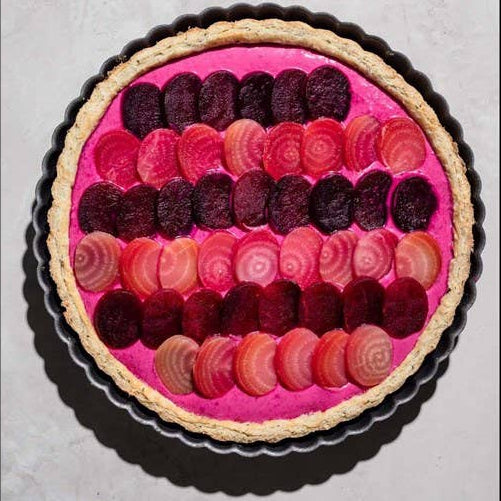 Pink tart with layered red and purple beets on a gray background