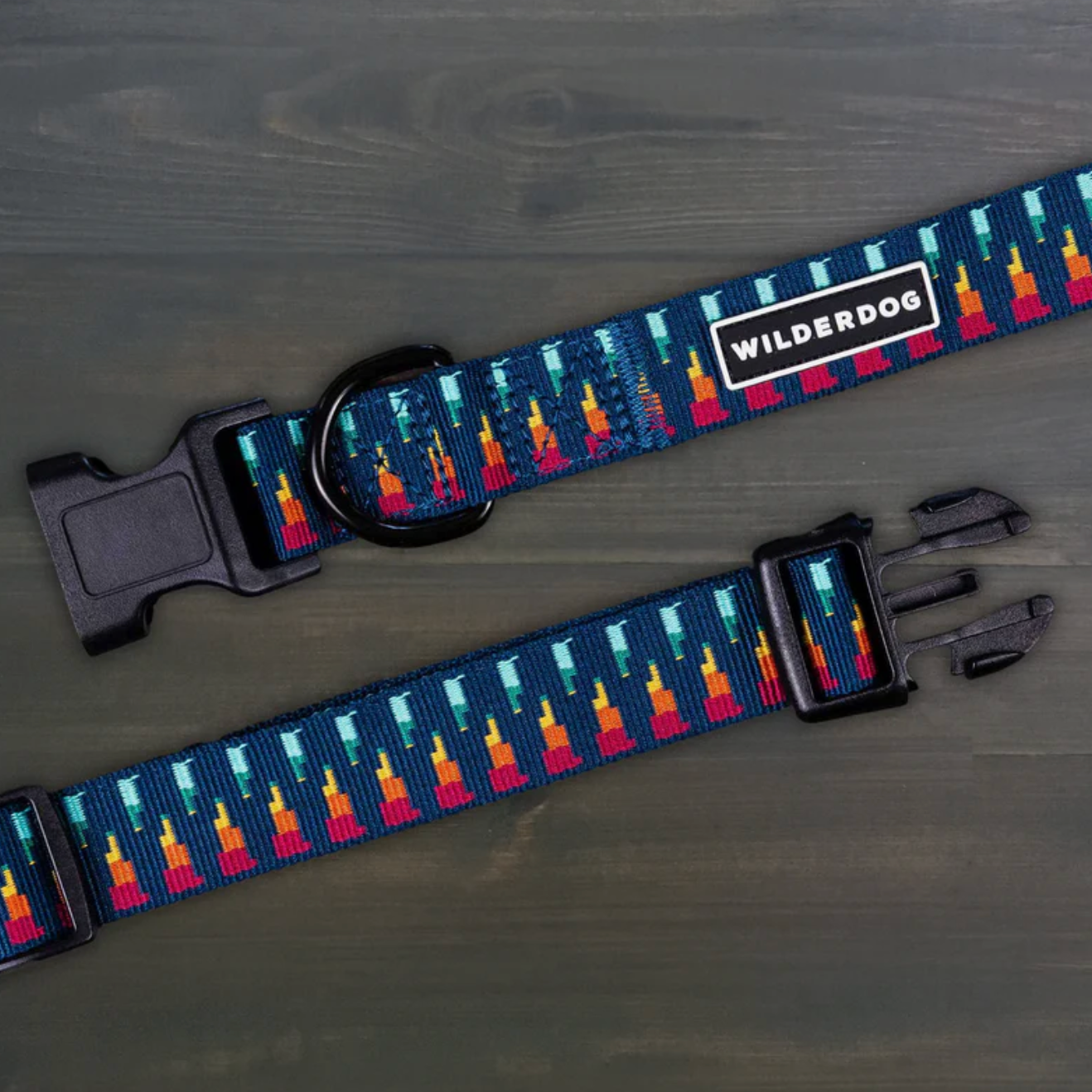 A dog collar with a navy blue background and a colorful geometric pattern in orange, yellow, and light blue. It features black plastic buckles and a white rectangular patch with the brand name 'WILDERDOG'.