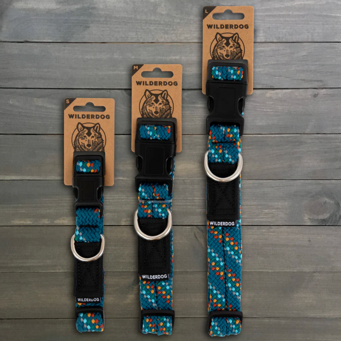 Three Wild Dog brand dog collars with blue, orange, and white patterned webbing and black plastic buckles, displayed on a gray wood plank background.