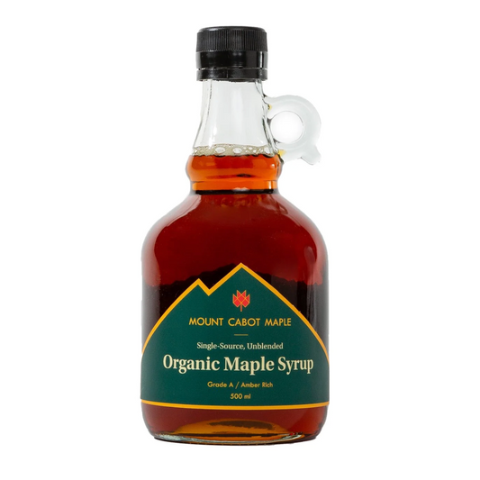 A 500 ml bottle of Mount Cabot Maple Organic Maple Syrup, featuring amber-brown syrup inside a clear glass bottle with a black cap and a green label.