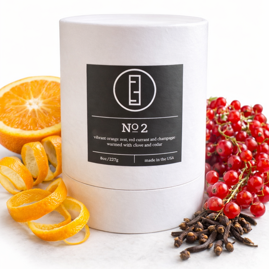Candle with a label surrounded by orange peels, red berries, and cloves on a white background